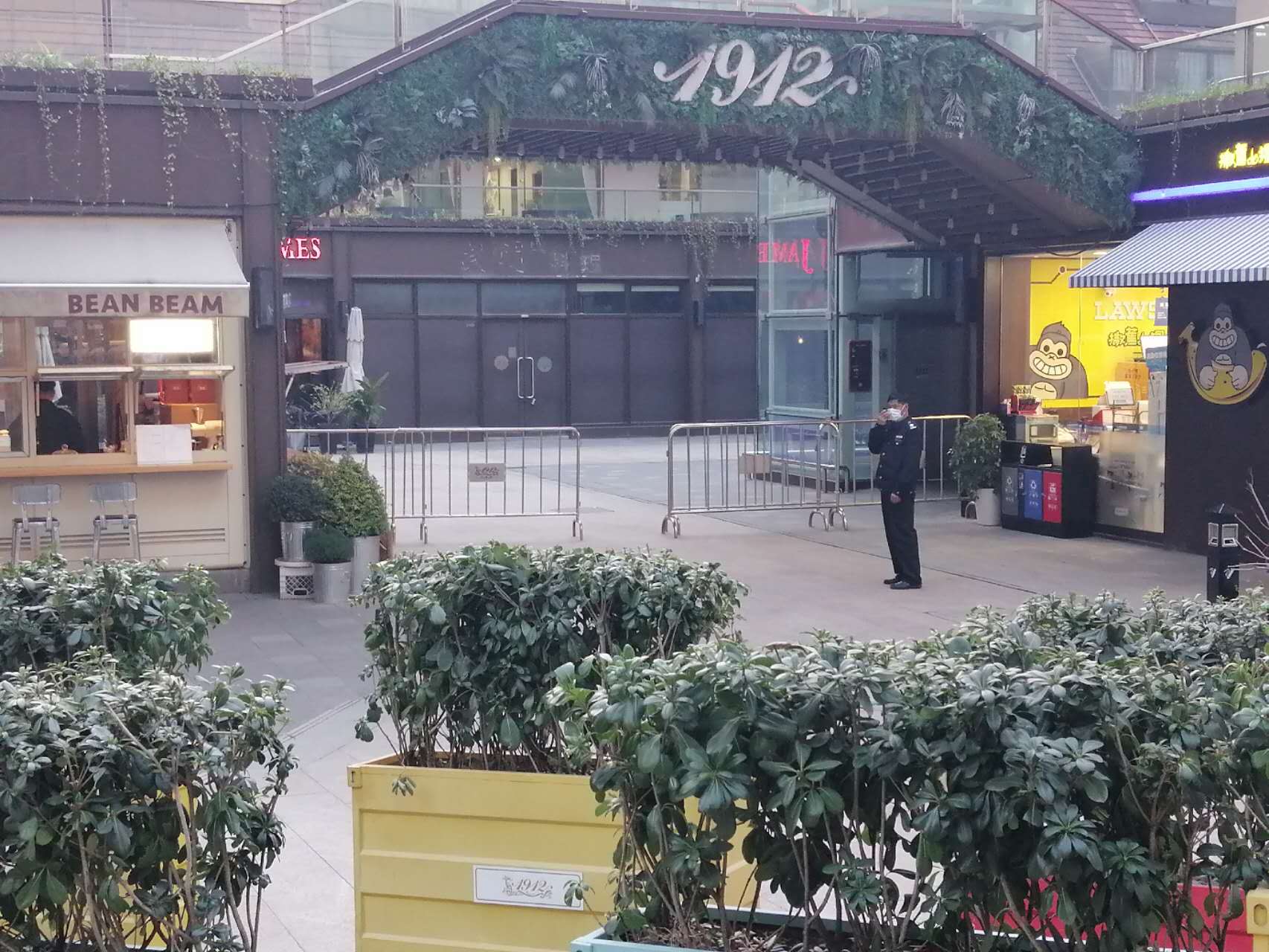 A shopping area marked 1912 with barriers and a masked attendant