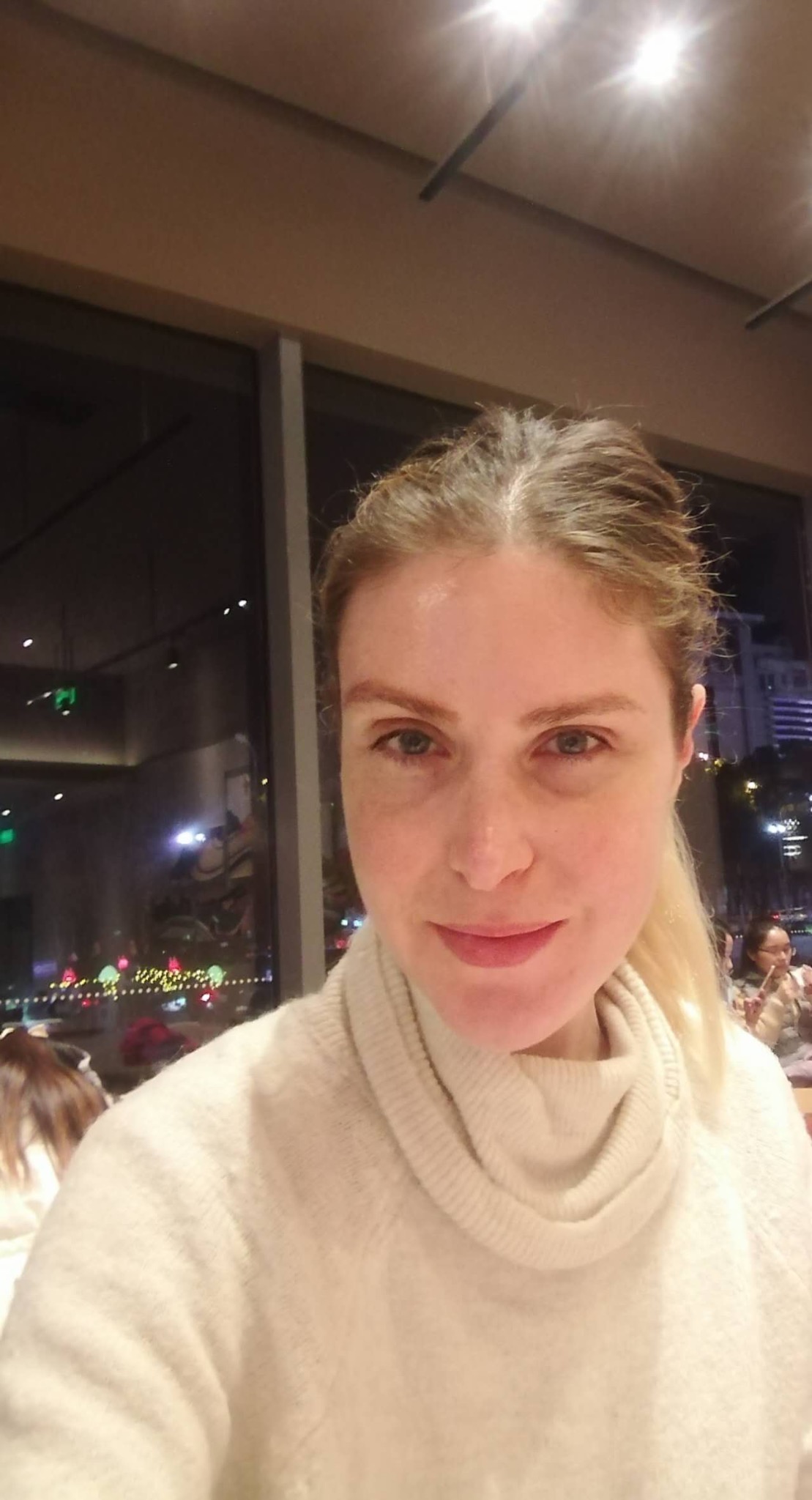 Rebecca seated by a café window at night