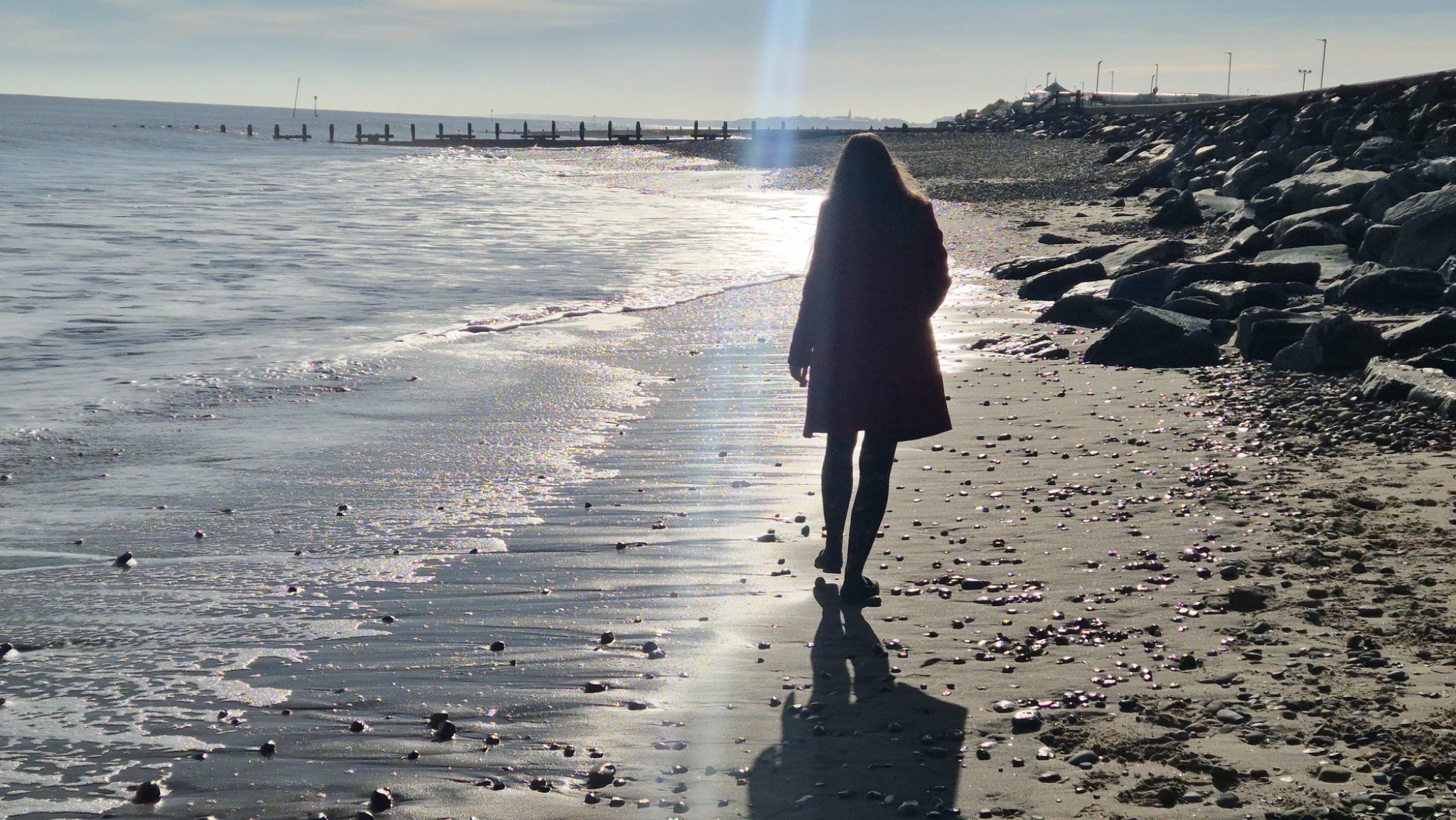 A woman walking along a sunlit beach beside the sea